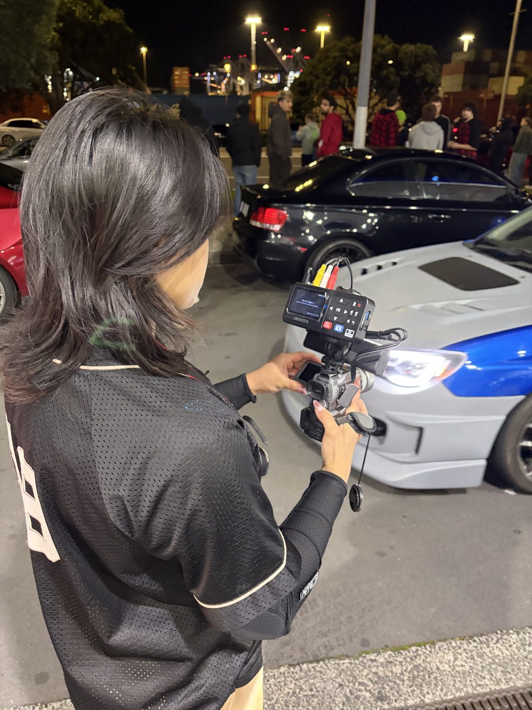 Clarissa filming with her camcorder rig at a night car meet