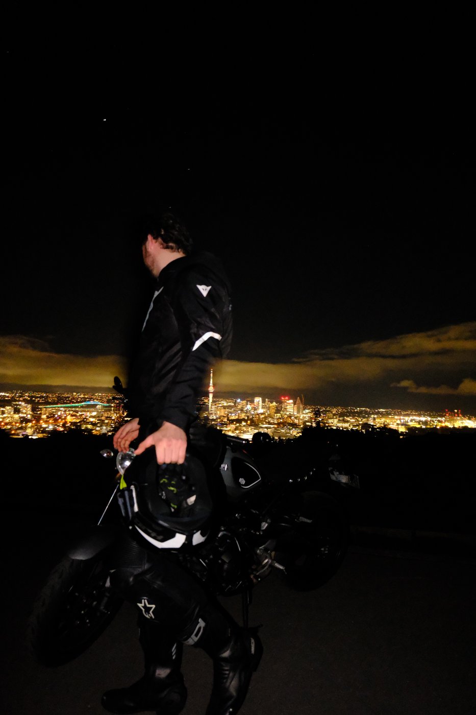 Rider with a cafe racer motorcycle overlooking the Auckland skyline at night